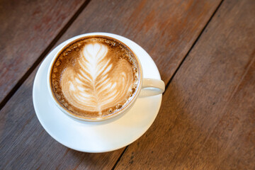 Hot coffee latte with latte art milk foam in cup mug on wood desk on top view. As breakfast In a coffee shop at the cafe,during business work concept,vintage style