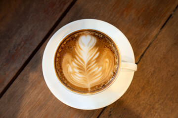 Hot coffee latte with latte art milk foam in cup mug on wood desk on top view. As breakfast In a...