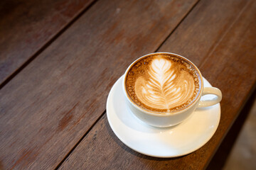 Hot coffee latte with latte art milk foam in cup mug on wood desk on top view. As breakfast In a coffee shop at the cafe,during business work concept,vintage style