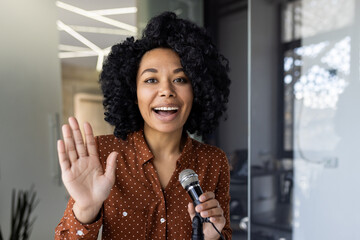 A cheerful African American businesswoman hosts a podcast, speaking into a microphone with a bright smile, conveying excitement and professionalism.