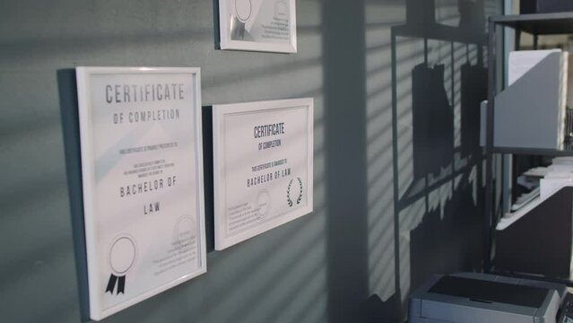 No people pull out footage of multiple certificates confirming getting bachelors degree in law on grey wall in office