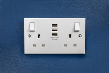 UK Double Plug Socket 3 with USB Chargers Pin on a Blue textured wall