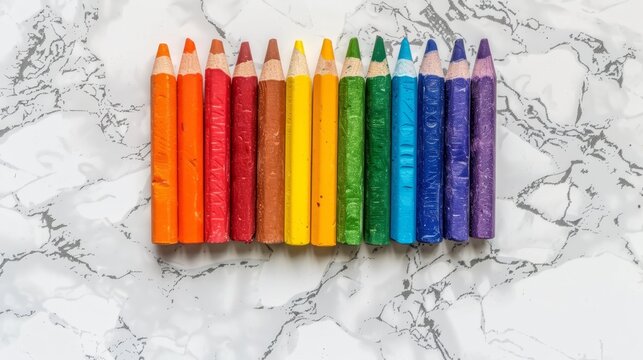  A row of colored pencils atop a white marble counter Nearby, a rainbow alignment of colored crayons sits in readiness