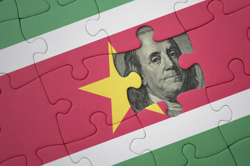 puzzle with the national flag of suriname and usa dollar banknote. finance concept