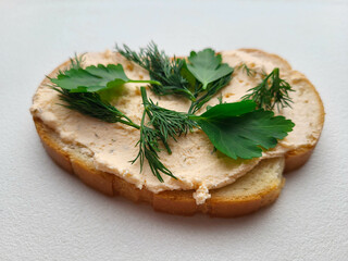 A piece of loaf is spread with soft cheese and dill and parsley are placed on top.