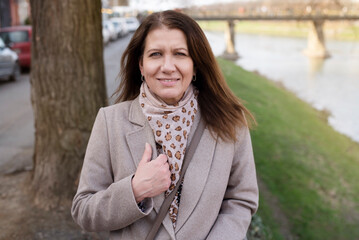 Portrait of a beautiful middle-aged woman in spring coat, woman walking along the river in the city and relaxing after a hard stressful day, emotional health concept
