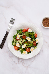 Fresh healthy vegetable salat: cucumber, tomatoes, spinach, couscous, quail eggs, flax seeds on marble background. Top view.