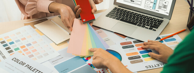 Cropped image of interior designer chooses color from color swatches while laptop displayed website...
