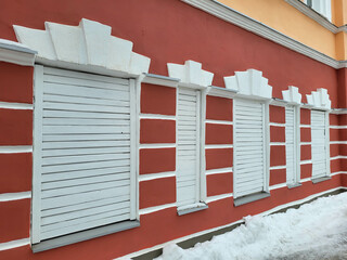 The red facade has white windows with closed shutters.