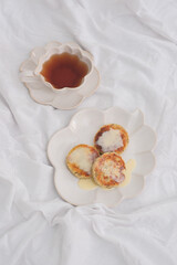 Cottage cheese fritters or syrniki served with syrop on white blanket.