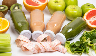 Healthy bottled smoothies among vegetables and fruits and measuring tape.