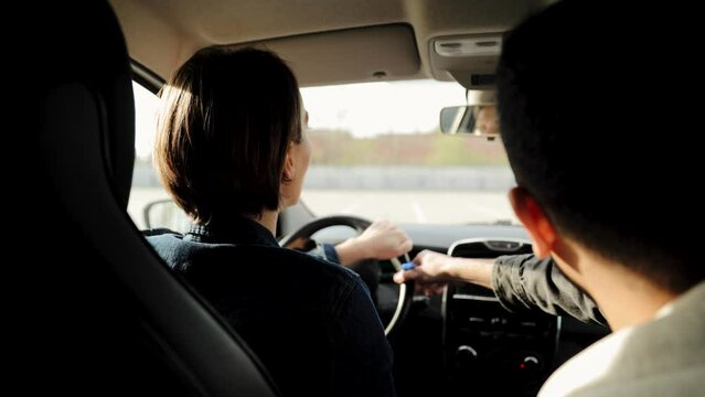 The man instructor teaches student to drive in the car. Backseat view of man and woman in car. Driver courses, driving school exam concept