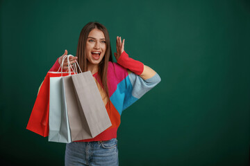 Crazy sale, shocked face, with shopping bags. Young woman is standing against green background in...