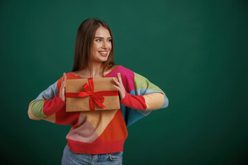 Holidays time. Holding gift box. Young woman is standing against green background in the studio