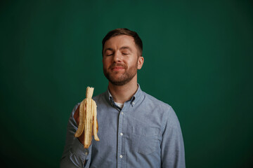 Holding banana. Man is standing against background in the studio
