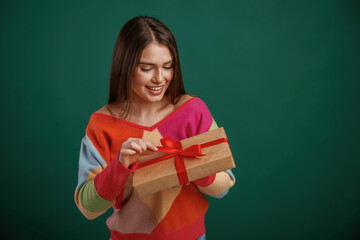 Holidays time. Holding gift box. Young woman is standing against green background in the studio