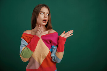 Thoughtful facial expression. Young woman is standing against green background in the studio