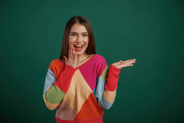 Showing by hand to the side, place for text. Young woman is standing against green background in the studio
