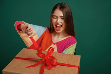 Opening the gift, anticipated. Young woman is standing against green background in the studio