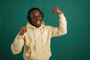 Listening to the music, dancing. African American man is standing against green background in the studio
