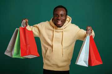 Shopping bags in hands, happy. African American man is standing against green background in the studio