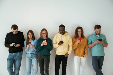 Busy by using smartphones. Group of young people are standing against white background