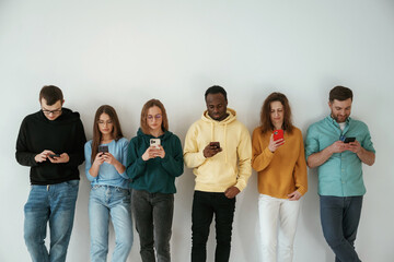 Obraz premium Busy by using smartphones. Group of young people are standing against white background