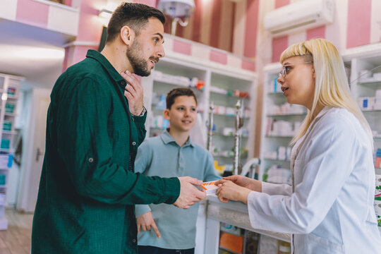 Cheerful young blonde pharmacist chemist woman giving vitamins, medicine to father and son. Having sore throat.
