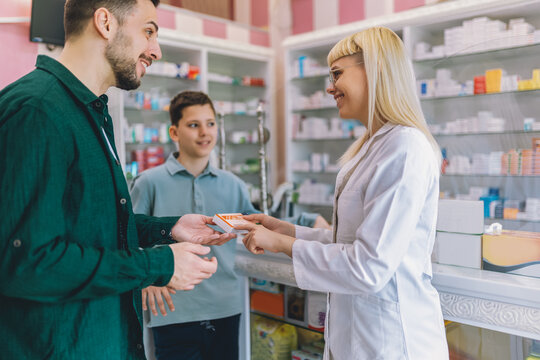 Cheerful young blonde pharmacist chemist woman giving vitamins, medicine to father and son.