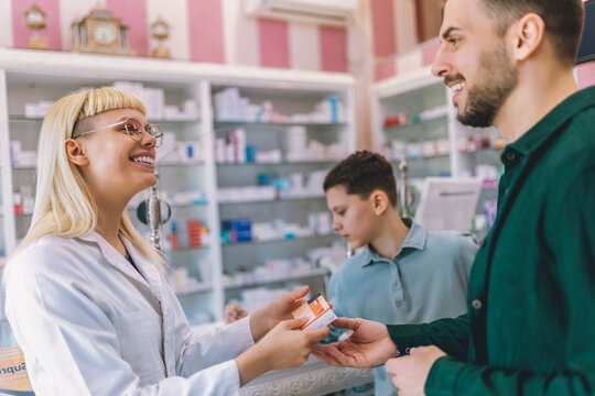 Cheerful young blonde pharmacist chemist woman giving vitamins, medicine to father and son.