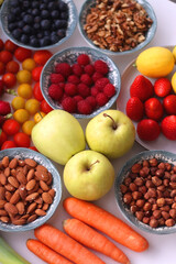 Apples, lemons, bananas, berries, carrots, leek, tomatoes, radishes, spinach and various nuts on white background. Healthy seasonal fruit and vegetable. Selective focus.