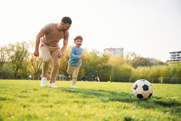 Playing soccer. Happy father with son are having fun on the field at summertime