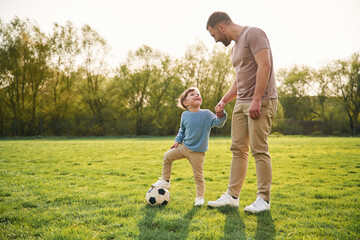 Game of soccer. With ball. Happy father with son are having fun on the field at summertime