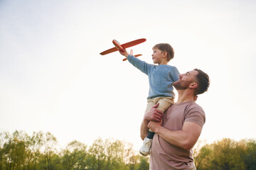Father is holding son that playing with toy plane