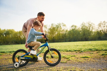 Fototapeta premium With bicycle, having fun. Happy father with son are on the field at summertime