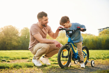 With bicycle, having fun. Happy father with son are on the field at summertime