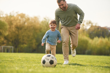 Learning to play soccer. Happy father with son are having fun on the field at summertime