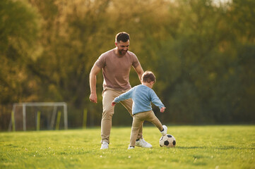 Learning to play soccer. Happy father with son are having fun on the field at summertime