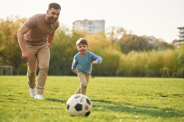 Learning to play soccer. Happy father with son are having fun on the field at summertime
