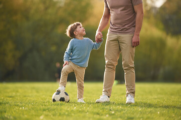 Teaching how to play a soccer. Happy father with son are having fun on the field at summertime