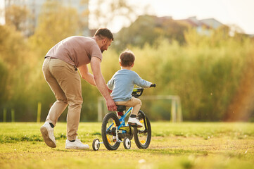 Riding on the blue bicycle. Happy father with son are having fun on the field at summertime