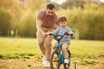 Blue bicycle, riding. Happy father with son are having fun on the field at summertime
