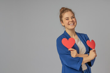 Positive girl with two paper hearts on a gray background on Valentine's Day