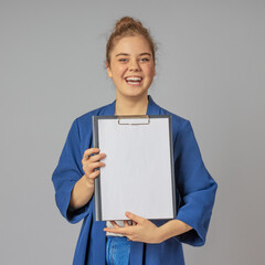 A girl with a wide smile shows a white piece of paper on a gray background to the camera