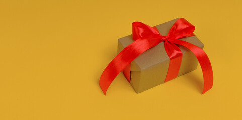 gift box wrapped in craft paper with red ribbon on yellow background, close-up