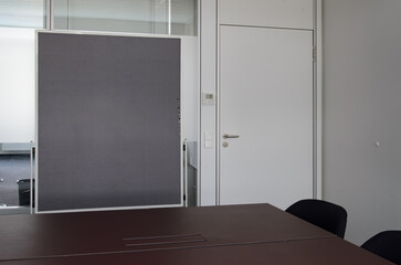 A black pinboard close-up in a conference room, closed door, dark brown table