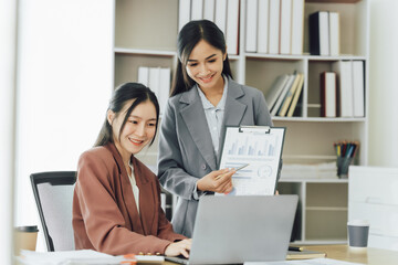 Two young Asian business woman talk, consult, discuss working with new startup project idea presentation analyze plan marketing and investment in the office.