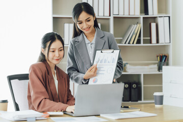 Two young Asian business woman talk, consult, discuss working with new startup project idea presentation analyze plan marketing and investment in the office.