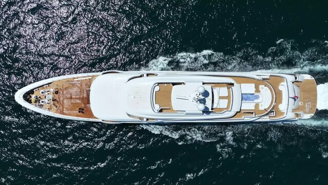 Aerial drone tracking top down video of beautiful modern super yacht with wooden deck and helipad cruising in high speed deep blue open ocean sea