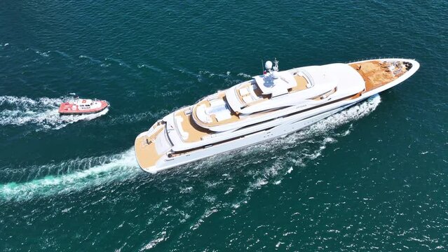 Aerial drone tracking photo of beautiful modern super yacht with wooden deck and helipad cruising in high speed deep blue open ocean sea
